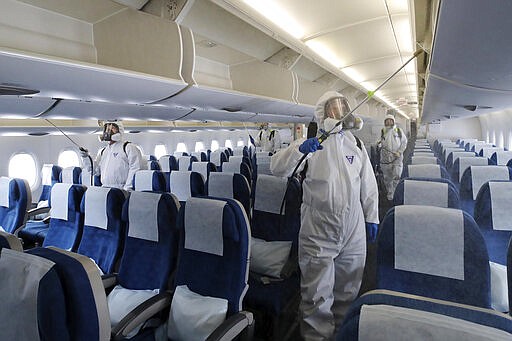 Workers wearing protective gears spray disinfectant inside a plane for New York as a precaution against the new coronavirus at Incheon International Airport in Incheon, South Korea, Wednesday, March 4, 2020. The coronavirus epidemic shifted increasingly westward toward the Middle East, Europe and the United States on Tuesday, with governments taking emergency steps to ease shortages of masks and other supplies for front-line doctors and nurses. (Suh Myoung-geon/Yonhap via AP)