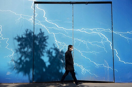 A man wearing a mask walks past a billboard depicting lightning in Beijing on Wednesday, March 4, 2020. The mushrooming outbreaks in other countries contrasted with optimism in China, where thousands of recovered patients were going home and the number of new infections dropped to the lowest level in more than six weeks. (AP Photo/Ng Han Guan)