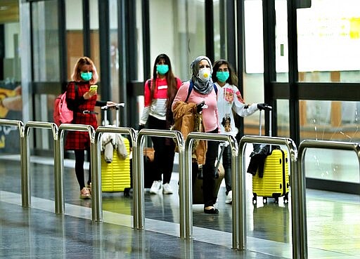 Passengers wearing protective masks walk with their belongings in Baghdad Airport, Iraq, Wednesday, March 4, 2020.  From religion to sports, countries were taking drastic and increasingly visible measures to curb the new coronavirus that first emerged in China and was spreading quickly through Europe, the Mideast and the Americas.  (AP Photo/Hadi Mizban)