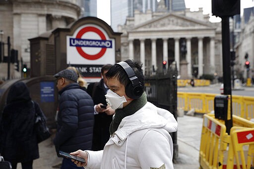 A man wearing a face mask walks past an entrance sign for Bank underground train station backdropped by the Royal Exchange building in London, Wednesday, March 4, 2020. British authorities laid out plans Tuesday to confront a COVID-19 epidemic, saying that the new coronavirus could spread within weeks from a few dozen confirmed cases to millions of infections, with thousands of people in the U.K. at risk of death. (AP Photo/Matt Dunham)