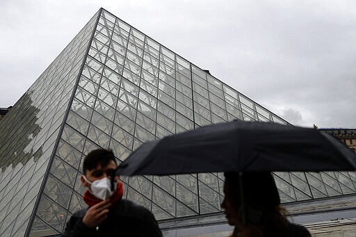 FILE - In this Monday, March 2, 2020 file photo, tourists wearing a mask walk away from the Louvre museum in Paris. Museum staffers who had stayed off the job since Sunday for fear of infection voted overwhelmingly on Wednesday to resume work. (AP Photo/Christophe Ena, File)