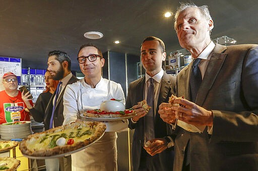 Italian Foreign Minister Luigi Di Maio, center, eats a pizza with French Ambassador to Rome Christian Masset, right, as pizza maker Gino Sorbillo holds up pizzas in his restaurant, in Rome, Wednesday, March 4, 2020. According to reports, Di Maio invited the French ambassador for a pizza after French channel Canal plus broadcast a satirical video of a fake Italian pizza maker coughing on a pizza and calling it &quot;Corona Pizza&quot;. (AP Photo/Andrew Medichini)