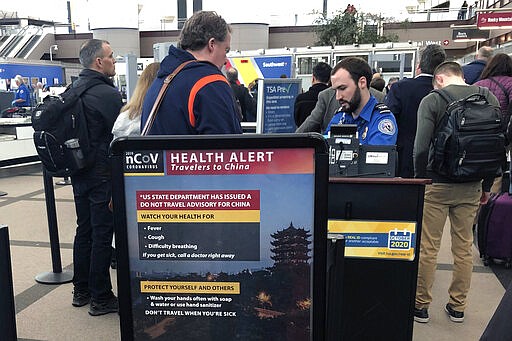 FILE - In this Monday, March 2, 2020 file photo, a health alert for people traveling to China is shown at a TSA security checkpoint at the Denver International Airport in Denver. A steep drop in business travel could be a gut punch to a tourism industry already reeling from the coronavirus outbreak, as big companies like Amazon try to keep employees healthy by banning trips.  (AP Photo/Charles Rex Arbogast, File)