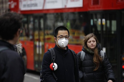 A man wearing a face mask walks backdropped by a red London bus across the street from the Bank of England in London, Wednesday, March 4, 2020. British authorities laid out plans Tuesday to confront a COVID-19 epidemic, saying that the new coronavirus could spread within weeks from a few dozen confirmed cases to millions of infections, with thousands of people in the U.K. at risk of death. (AP Photo/Matt Dunham)