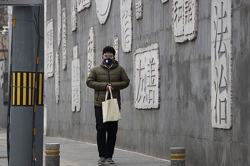 In this Feb. 25, 2020, photo, a resident wearing a mask walks outside a closed school with a mural depicting keywords including at right &quot;Rule of law&quot; in Beijing. Chinese schools turning to online learning during a virus outbreak are running into the country's ubiquitous and often arbitrary internet censorship. (AP Photo/Ng Han Guan)