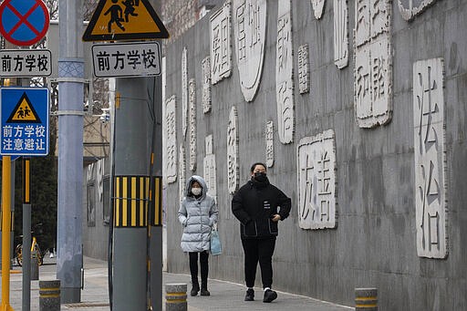 In this Feb. 25, 2020, photo, residents walk outside a closed school with a mural depicting keywords including at right &quot;Rule of law&quot; in Beijing. Chinese schools turning to online learning during a virus outbreak are running into the country's ubiquitous and often arbitrary internet censorship. (AP Photo/Ng Han Guan)