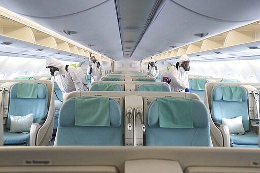 Workers wearing protective gears spray disinfectant inside an airplane for New York as a precaution against the new coronavirus at Incheon International Airport in Incheon, South Korea, Wednesday, March 4, 2020. The coronavirus epidemic shifted increasingly westward toward the Middle East, Europe and the United States on Tuesday, with governments taking emergency steps to ease shortages of masks and other supplies for front-line doctors and nurses. (Suh Myoung-geon/Yonhap via AP)