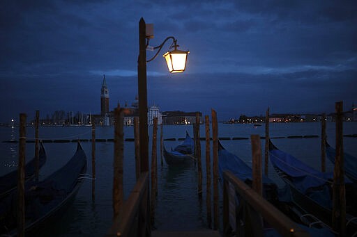 Boats sail along the lagoon next to parked gondolas in Venice, Italy, Tuesday, March 3, 2020. Venice in the time of coronavirus is a shell of itself, with empty piazzas, shuttered basilicas and gondoliers idling their days away. A UNESCO world heritage site, it had already been brought to its knees last year, when near-record high tides flooded a lagoon city used to frequent spells of &quot;aqua alta.&quot; (AP Photo/Francisco Seco)