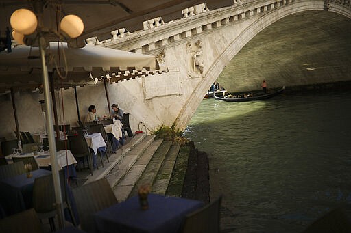 Tourists eat a meal on an almost empty restaurant terrace in Venice, Italy, Friday, Feb. 28, 2020. Venice in the time of coronavirus is a shell of itself, with empty piazzas, shuttered basilicas and gondoliers idling their days away. Venice, a UNESCO world heritage site, had already been brought to its knees last year, when near-record high tides flooded a lagoon city used to frequent spells of &quot;aqua alta.&quot; (AP Photo/Francisco Seco)