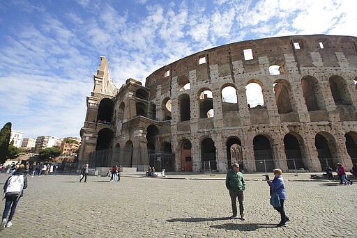 People walk by the Colosseum in Rome, Thursday, March 5, 2020. Italy closed all schools and universities Wednesday and barred fans from all sporting events for the next few weeks as governments trying to curb the spread of the coronavirus resorted to increasingly sweeping measures, transforming the way people work, shop, pray and amuse themselves. (AP Photo/Andrew Medichini)