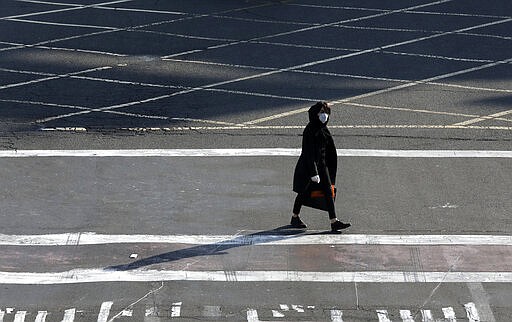 A woman wearing a face mask and gloves crosses an intersection in northern Tehran, Iran, Wednesday, March 4, 2020. With deaths spiking in Iran and Italy and infections spreading quickly through Europe, the Mideast and the Americas, countries were considering new drastic measures to curb the new coronavirus that first emerged in China. (AP Photo/Vahid Salemi)