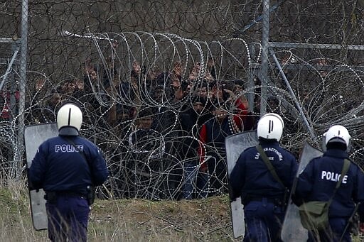 Greek riot police guard as migrants stand on a fence as they try to enter Greece from Turkey at the Greek-Turkish border in Kastanies on Wednesday, March 4, 2020. Facing a potential wave of nearly a million people fleeing fighting in northern Syria, Turkey has thrown open its borders with Greece to thousands of refugees and other migrants trying to enter Europe, and has threatened to send &quot;millions&quot; more. (AP Photo/Giannis Papanikos)