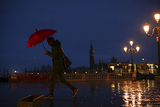 A man shelters against the rain and windy with an umbrella in Venice, Monday, March 2, 2020. Venice in the time of coronavirus is a shell of itself, with empty piazzas, shuttered basilicas and gondoliers idling their days away. Venice, a UNESCO world heritage site, had already been brought to its knees last year, when near-record high tides flooded a lagoon city used to frequent spells of &quot;aqua alta.&quot; (AP Photo/Francisco Seco)