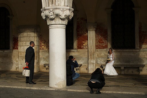 A woman wearing a bridal dress poses for photographs near St. Mark's square in Venice, Italy, Tuesday, March 3, 2020. Venice in the time of coronavirus is a shell of itself, with empty piazzas, shuttered basilicas and gondoliers idling their days away. Venice, a UNESCO world heritage site, had already been brought to its knees last year, when near-record high tides flooded a lagoon city used to frequent spells of &quot;aqua alta.&quot; (AP Photo/Francisco Seco)