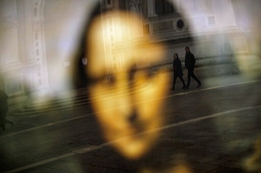 People walk past a reflection of the Mona Lisa in the Leonardo da Vinci museum, temporary closed due to the COVID-19 virus outbreak, in Venice, Saturday, Feb. 29, 2020. (AP Photo/Francisco Seco)