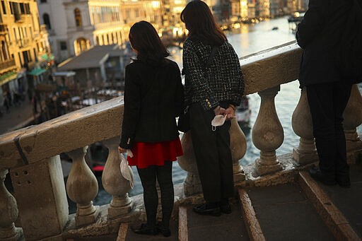 Tourists hold their protective masks as they pose for a photograph at the Rialto bridge in Venice, Italy, Friday, Feb. 28, 2020. Venice in the time of coronavirus is a shell of itself, with empty piazzas, shuttered basilicas and gondoliers idling their days away. The city has remained quiet ever since the outbreak, with only intrepid tourists wearing a different type of mask _ surgical _ remaining and taking advantage of a city that otherwise would be jammed. (AP Photo/Francisco Seco)