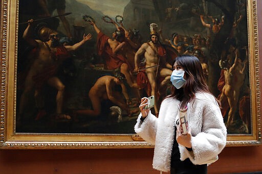 Masked tourist walks by an oil on canvas of 1814 entitled Leonidas at Thermopylae, by Jacques Louis David, at the Louvre Museum in Paris, Thursday, March 5, 2020. With the COVID-19 virus taking firmer hold in Europe, the continent is facing the same complications seen in Asia weeks ago. (AP Photo/Francois Mori)