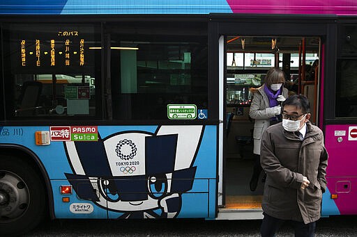 Passengers wearing masks get off a bus with the livery of Miraitowa, the official mascot of the Tokyo 2020 Olympics, in Tokyo, Thursday, March 5, 2020. Despite worldwide concern and speculation about whether the fast-spreading virus outbreak will affect the Tokyo Olympics, the IOC's leadership is not joining in the debate. (AP Photo/Jae C. Hong)