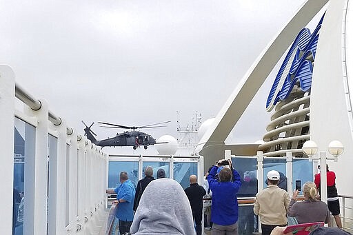 CORRECTS FROM COAST GUARD TO NATIONAL GUARD HELICOPTER- In this photo provided by Michele Smith, passengers look on as a National Guard helicopter hovers above the Grand Princess cruise ship Thursday, March 5, 2020, off the California coast. Scrambling to keep the coronavirus at bay, officials ordered a cruise ship with about 3,500 people aboard to stay back from the California coast Thursday until passengers and crew can be tested, after a traveler from its previous voyage died of the disease and at least two others became infected. A Coast Guard helicopter lowered test kits onto the 951-foot (290-meter) Grand Princess by rope as the vessel lay at anchor off Northern California, and authorities said the results would be available on Friday. Princess Cruise Lines said fewer than 100 people aboard had been identified for testing. (Michele Smith via AP)