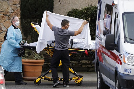 A staff member blocks the view as a person is taken by a stretcher to a waiting ambulance from a nursing facility where more than 50 people are sick and being tested for the COVID-19 virus, Saturday, Feb. 29, 2020, in Kirkland, Wash. (AP Photo/Elaine Thompson)