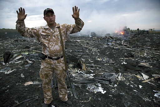 FILE- In this Thursday, July 17, 2014 file photo, a man gestures at a crash site of a passenger plane near the village of Grabovo, Ukraine. United by grief across oceans and continents, families who lost loved ones when Malaysia Airlines Flight 17 was shot down in 2014 hope that a trial starting next week will finally deliver them something that has remained elusive ever since: The truth. (AP Photo/Dmitry Lovetsky, File)