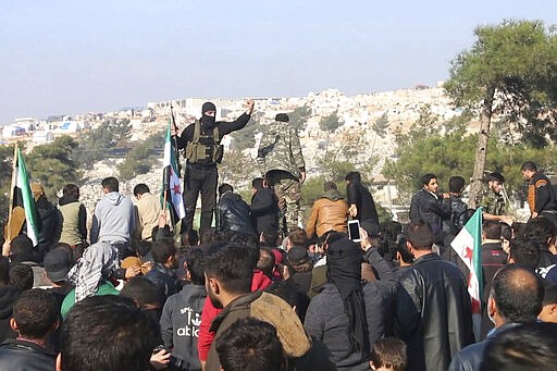 FILE - In this frame grab from video taken on Dec. 20, 2019, militants of the al-Qaida-linked Hayat Tahrir al-Sham try to disperse people who have gathered at the Bab al-Hawa border gate to protest the ongoing bombing campaign in Syria's rebel-controlled Idlib province by the government and its Russian ally. Intermingled among 3 million civilians under siege in the Syrian government's assault on the last opposition stronghold are tens of thousands of al-Qaida-linked fighters and other militants who came from around the world to take part in the country's civil war. (AP Photo, File)