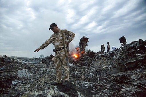 FILE- In this July 17, 2014, file photo, people walk amongst the debris at the crash site of MH17 passenger plane near the village of Grabovo, Ukraine, that left 298 people killed. United by grief across oceans and continents, families who lost loved ones when Malaysia Airlines Flight 17 was shot down in 2014 hope that a trial starting next week will finally deliver them something that has remained elusive ever since: The truth. (AP Photo/Dmitry Lovetsky, File)