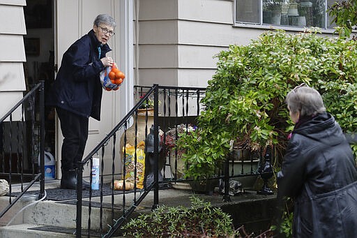 Pat McCauley gathers groceries and other items left on her porch by her daughter, Cheri Chandler, right, at her home, Friday, March 6, 2020, in Kirkland, Wash. Pat and her husband Bob have been self-quarantined in their home during the past week due to having visited friends at the Life Care Center nursing home &#151; which has become the epicenter of the outbreak of the COVID-19 coronavirus in Washington state &#151; several times in February. (AP Photo/Ted S. Warren)