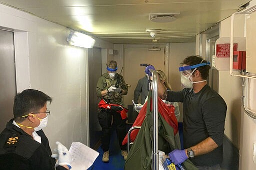 In this Thursday, March 5, 2020, photo, released by the California National Guard, Guardian Angels, a group of medical personnel with the 129th Rescue Wing, working alongside individuals from the Centers for Disease Control and Prevention, don protective equipment after delivering virus testing kits to the Grand Princess cruise ship off the coast of California. Passengers on a cruise ship off the California coast were instructed to stay in their cabins as they awaited test results Friday that could show whether the coronavirus is circulating among the more than 3,500 people aboard. (Chief Master Sgt. Seth Zweben/California National Guard via AP)