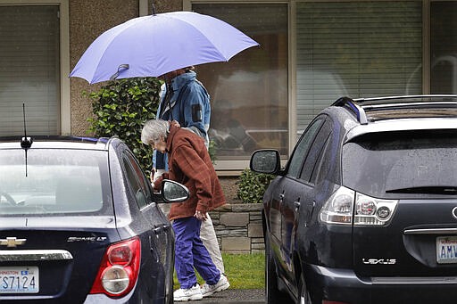 Dorothy Campbell walks with her son Charlie Campbell as her husband, Gene Campbell watches from the window of his room at the Life Care Center in Kirkland, Wash., Friday, March 6, 2020. Dorothy and her son came to visit Gene Friday as he is isolated in the facility that has been the epicenter of the outbreak of the the COVID-19 coronavirus. Charlie later told reporters that his father, who had not yet been tested, was showing symptoms of the virus and would be taken to a hospital. (AP Photo/Ted S. Warren)