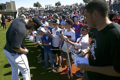 Cleveland Indians' Mike Freeman, left, signs autographs for fans as a Goodyear Stadium employee holds a container of pens and autograph cards prior to the team's spring training baseball game against the Chicago Cubs on Saturday, March 7, 2020, in Goodyear, Ariz. The stadium offered the items for players to sign autographs as a precaution for the coronavirus. (AP Photo/Ross D. Franklin)