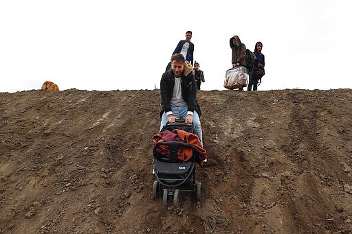 A migrant hods a baby-stroller as he comes down a slope in Edirne near the Turkish-Greek border on Thursday, March 5, 2020. Turkey has vowed to seek justice for a migrant it says was killed on the border with Greece after Greek authorities fired tear gas and stun grenades to push back dozens of people attempting to cross over. Greece had denied that anyone was killed in the clashes. (AP Photo/Darko Bandic)