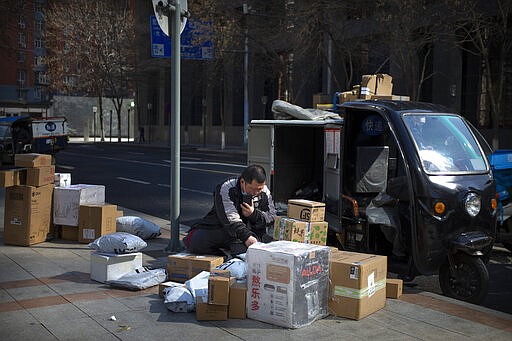 A courier wears a face mask as he sorts packages outside of a residential neighborhood in Beijing, Saturday, March 7, 2020. China's exports fell by double digits in January and February as anti-virus controls closed factories, while imports sank by a smaller margin. (AP Photo/Mark Schiefelbein)