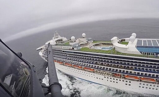 In this image from video, provided by the California National Guard, a helicopter carrying airmen with the 129th Rescue Wing flies over the Grand Princess cruise ship off the coast of California Thursday, March 5, 2020. Scrambling to keep the coronavirus at bay, officials ordered a cruise ship with 3,500 people aboard to stay back from the California coast Thursday until passengers and crew can be tested, after a traveler from its previous voyage died of the disease and at least two others became infected. Airmen lowered test kits onto the 951-foot (290-meter) Grand Princess by rope as the vessel lay at anchor off Northern California, and authorities said the results would be available on Friday. Princess Cruise Lines said fewer than 100 people aboard had been identified for testing. (California National Guard via AP)