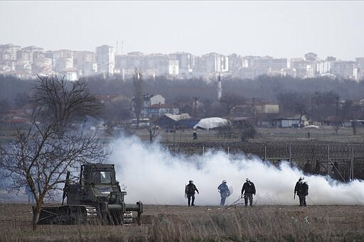 Greek police guard as migrants gather at a border fence on the Turkish side, during clashes at the Greek-Turkish border in Kastanies, Evros region, on Saturday, March 7, 2020. Thousands of refugees and other migrants have been trying to get into EU member Greece in the past week after Turkey declared that its previously guarded borders with Europe were open. (AP Photo/Giannis Papanikos)