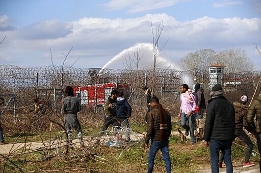 Greek firefighters spray water as migrants stand near a border fence on the Turkish side during clashes with the Greek riot police at the Turkish-Greek border in Pazarkule, Edirne region, on Saturday, March 7, 2020. Thousands of refugees and other migrants have been trying to get into EU member Greece in the past week after Turkey declared that its previously guarded borders with Europe were open. (AP Photo/Darko Bandic)