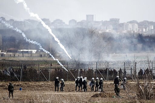 Greek police and army guard as migrants gather at a border fence on the Turkish side, during clashes at the Greek-Turkish border in Kastanies, Evros region, on Saturday, March 7, 2020. Thousands of refugees and other migrants have been trying to get into EU member Greece in the past week after Turkey declared that its previously guarded borders with Europe were open. (AP Photo/Giannis Papanikos)