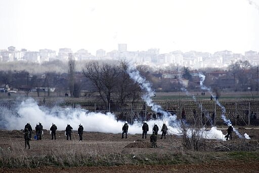 Greek police and army guard as migrants gather at a border fence on the Turkish side, during clashes at the Greek-Turkish border in Kastanies, Evros region, on Saturday, March 7, 2020. Thousands of refugees and other migrants have been trying to get into EU member Greece in the past week after Turkey declared that its previously guarded borders with Europe were open. (AP Photo/Giannis Papanikos)