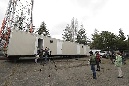 Reporters and photographers work Tuesday, March 3, 2020, at the site in South Seattle where King County will be placing several temporary housing units like the one shown here to house patients undergoing treatment and isolation in response to the COVID-19 coronavirus. (AP Photo/Ted S. Warren)