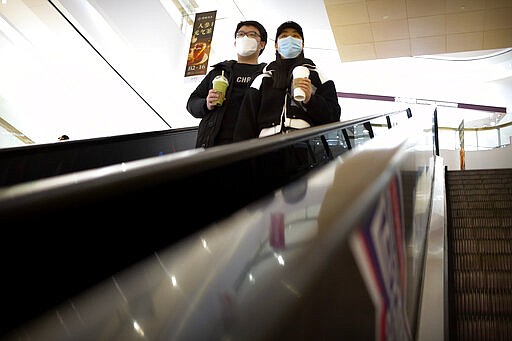 A couple wear face masks as they ride an escalator at a shopping mall in Beijing, Saturday, March 7, 2020. Crossing more borders, the new coronavirus hit a milestone, infecting more than 100,000 people worldwide as it wove itself deeper into the daily lives of millions, infecting the powerful, the unprotected poor and vast masses in between. (AP Photo/Mark Schiefelbein)