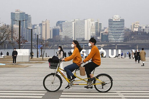 A couple wearing face masks rides a bicycle at a park in Seoul, South Korea, Saturday, March 7, 2020. The number of infections of the COVID-19 disease spread around the globe. (AP Photo/Ahn Young-joon)