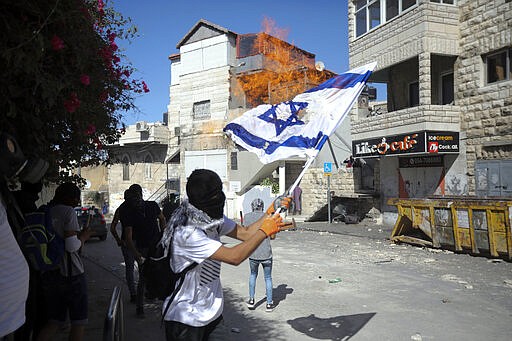 FILE - In this June 28, 2019 file photo, Palestinians burn an Israeli flag during clashes with Israeli police in East Jerusalem's Palestinian neighborhood of Issawiya, a day after a Palestinian was shot and killed by police during a protest in the same neighborhood. Nearly every day for the last nine months Israeli police have stormed into Issawiya in a campaign they say is needed to maintain law and order. Rights groups say that in addition to searching houses and issuing fines, they have detained hundreds of people &#151; some as young as 10, on suspicion of stone-throwing. The operations frequently ignite clashes, with local youths throwing rocks and firebombs. Residents and human rights groups say the provocative raids have created an atmosphere of terror, with parents afraid to let their children play outside. (AP Photo/Mahmoud Illean)