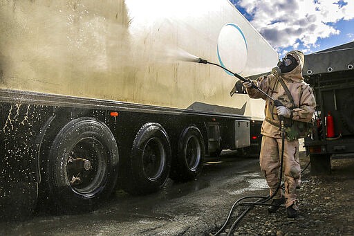 In this Sunday, March 1, 2020, photo, a Revolutionary Guard member disinfects a truck to help prevent the spread of the new coronavirus in the city of Sanandaj, western Iran. Wearing gas masks and waterproof fatigues, members of Iran's Revolutionary Guard now spray down streets and hospitals with disinfectants as the Islamic Republic faces one of the world's worst outbreaks of the new coronavirus. (Keyvan Firouzei/Tasnim News Agency via AP)