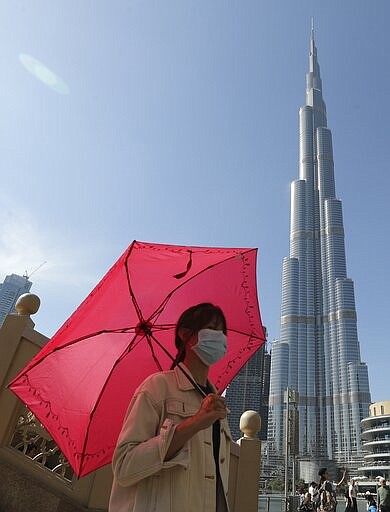 In this Thursday, Jan. 30, 2020, photo, a Chinese woman wearing a protective face mask walks under the world's tallest tower, Burj Khalifa, in Dubai, United Arab Emirates. The World Health Organization declared the outbreak sparked by a new virus in China that has been exported to more than a dozen countries as a global emergency Thursday after the number of cases spiked tenfold in a week. (AP Photo/Kamran Jebreili)