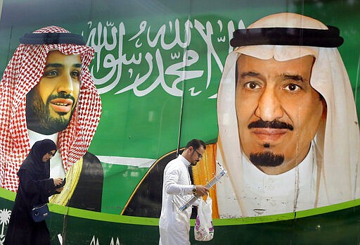 People walk past a banner showing Saudi King Salman, right, and his Crown Prince Mohammed bin Salman, outside a mall in Jiddah, Saudi Arabia, Saturday, March 7, 2020. (AP Photo/Amr Nabil)