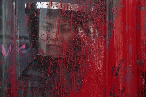 A police officer stands behind her riot shield covered in red paint during an International Women's Day march in Mexico City's main square, the Zocalo, Sunday, March 8, 2020. Protests against gender violence in Mexico have intensified in recent years amid an increase in killings of women and girls.(AP Photo/Rebecca Blackwell)