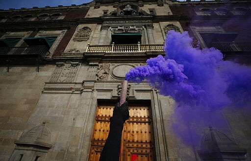 A woman holds up a smoke candle at the door of the National Palace during an International Women's Day march in Mexico City's main square, the Zocalo, Sunday, March 8, 2020. Protests against gender violence in Mexico have intensified in recent years amid an increase in killings of women and girls.(AP Photo/Rebecca Blackwell)