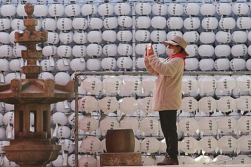 A visitor wearing a face mask takes photos near lanterns in preparation for the upcoming birthday of Buddha on April 30 at the Chogyesa temple in Seoul, South Korea, Sunday, March 8, 2020. The number of infections of the COVID-19 disease continues spread around the globe. (AP Photo/Ahn Young-joon)