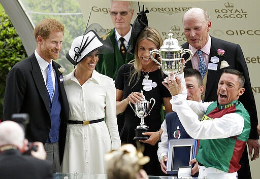 FILE - In this Tuesday, June 19, 2018 file photo, Britain's Prince Harry and Meghan, Duchess of Sussex present the trophy for the St James's Palace Stakes to Frankie Dettori, right, on the first day of the Royal Ascot horse race meeting in Ascot, England. Prince Harry and his wife, Meghan, are fulfilling their last royal commitment Monday March 9, 2020 when they appear at the annual Commonwealth Service at Westminster Abbey. It is the last time they will be seen at work with the entire Windsor clan before they fly off into self-imposed exile in North America. (AP Photo/Tim Ireland, file)