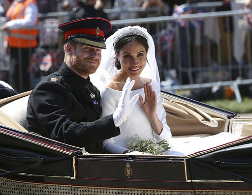 FILE - In this Saturday, May 19, 2018 file photo, Britain's Prince Harry and Meghan Markle ride in an open-topped carriage after their wedding ceremony at St. George's Chapel in Windsor Castle in Windsor, England. Prince Harry and his wife, Meghan, are fulfilling their last royal commitment Monday March 9, 2020 when they appear at the annual Commonwealth Service at Westminster Abbey. It is the last time they will be seen at work with the entire Windsor clan before they fly off into self-imposed exile in North America. (Aaron Chown/pool photo via AP, file)